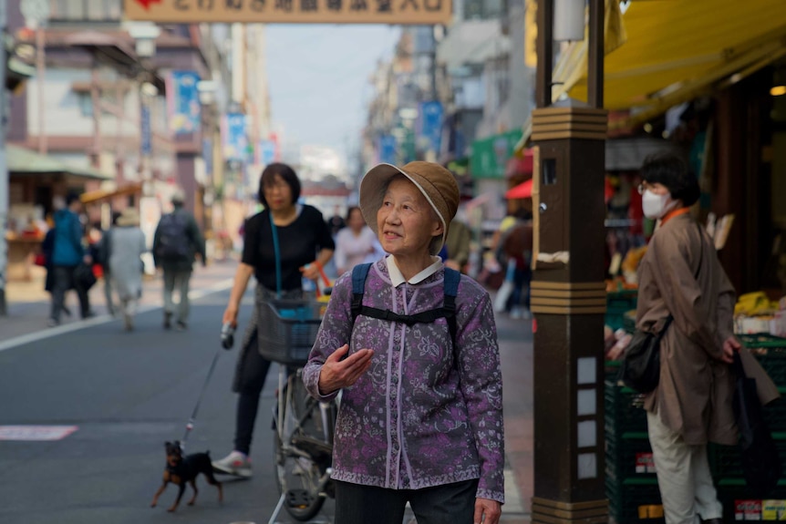 An elderly woman stands on a busy street