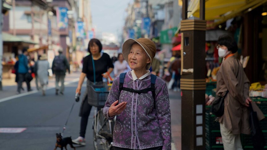 An elderly woman stands on a busy street