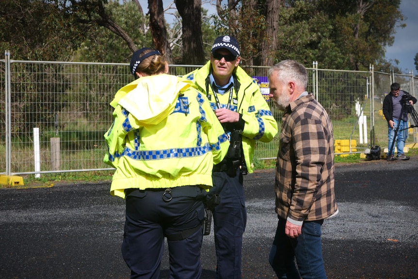 Police speak with a man in front of a row of fences
