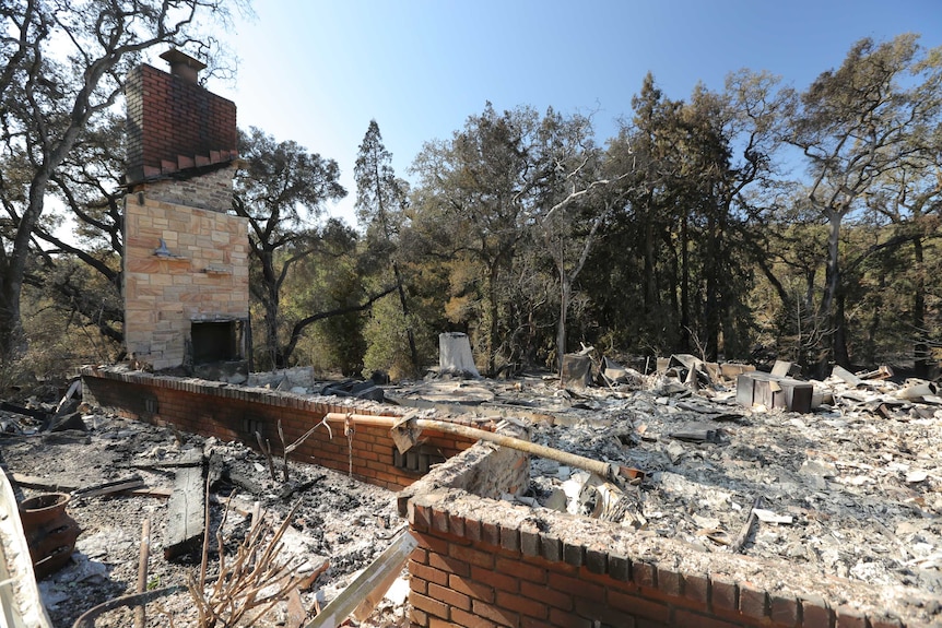 The sandstone and brick fireplace stands upright, surrounded by household items reduced to ash and rubble.