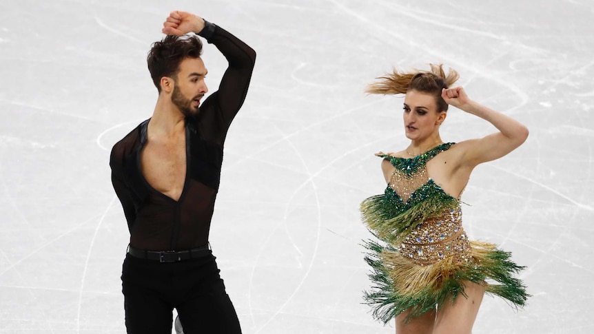 Guillaume looks towards the right shoulder strap of his partner's costume as it starts to slip off her shoulder as they dance