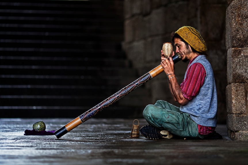A man plays didgeridoo while sitting on the ground
