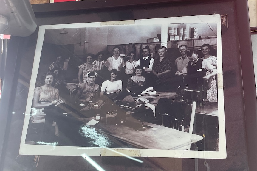 An olden photo of more than a dozen people in a work shop stand by eachother