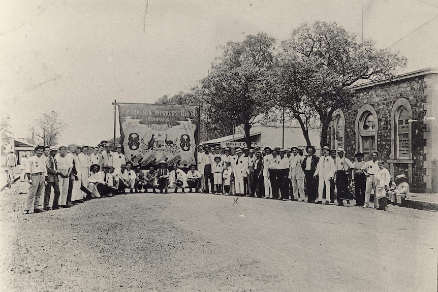 A black and white photo of workers with a banner in the middle of the street.