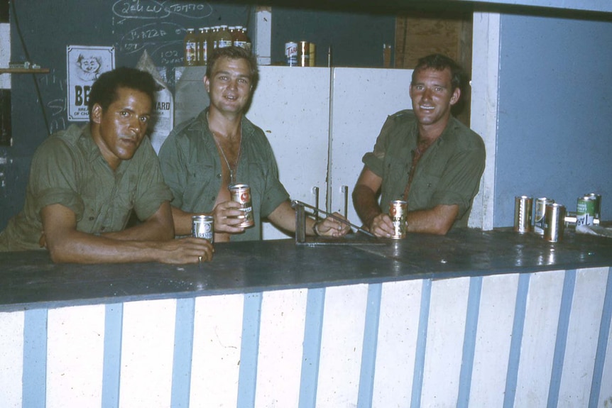 Three men stand behind a bar with drinks in hand.