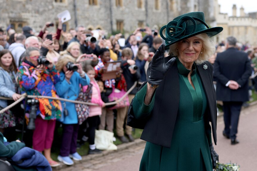 La reina Camilla saluda con un vestido de abrigo verde y un sombrero.