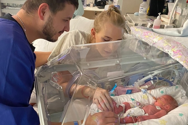 Kristen Meadows and her partner look at their premature baby girl in a hospital incubator