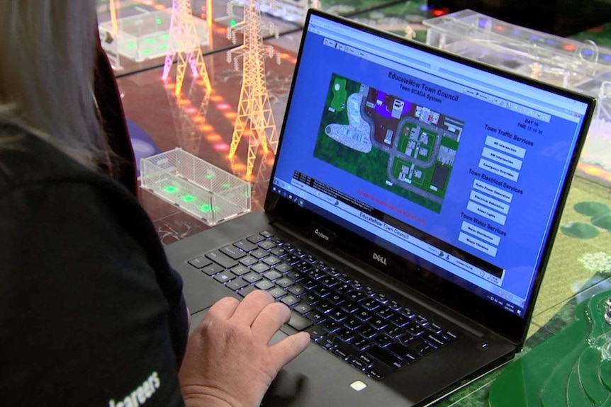 A laptop that says "EducateNow Town Council" on a table that shows bright lights and power lines.