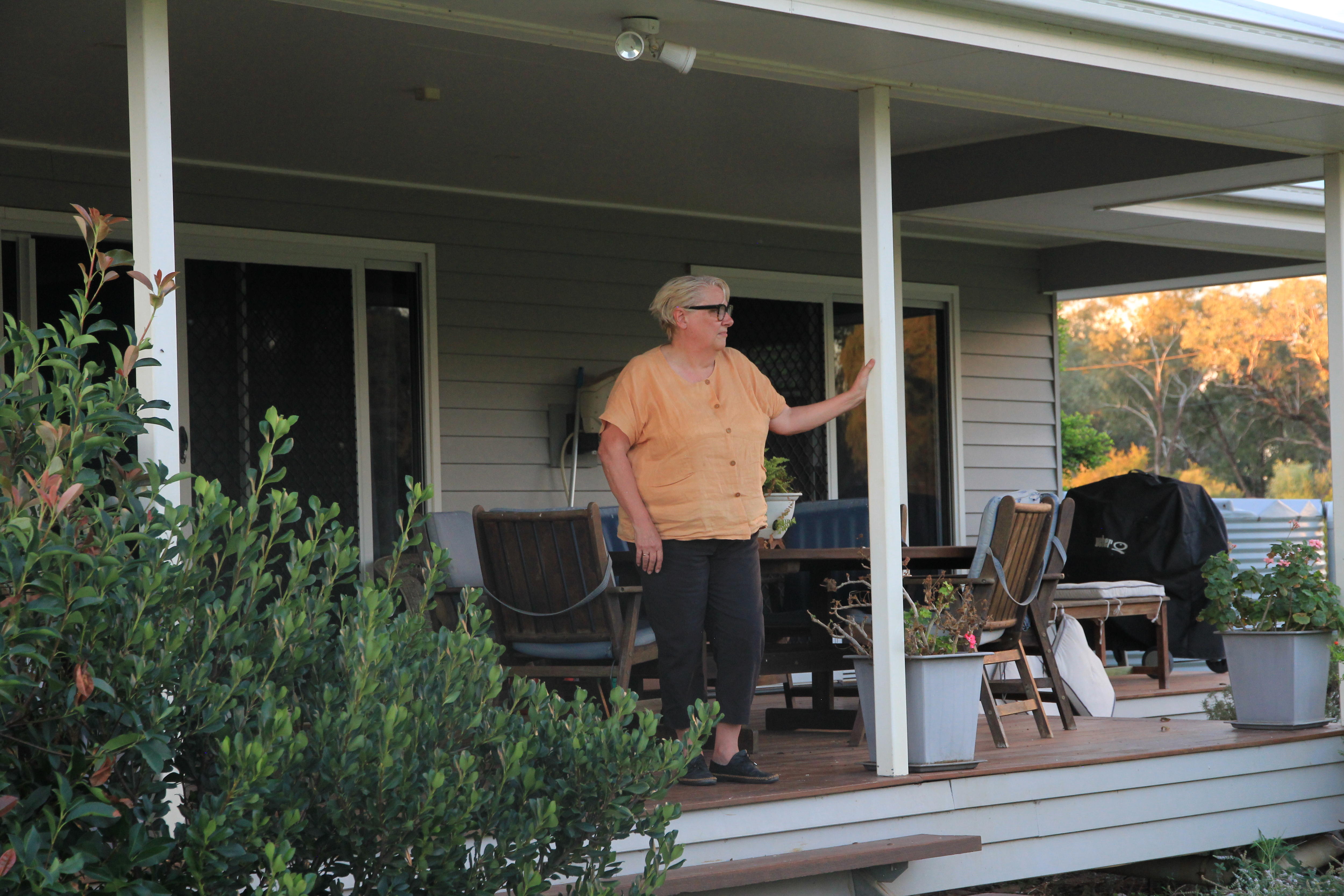 Mujer con pelo corto gris y camisa naranja se encuentra en su porche y mira