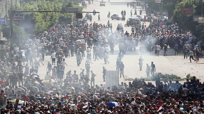 A crowd of people are in an Egyptian street shrouded in smoke.