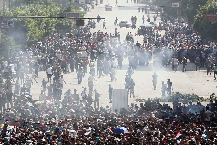 A crowd of people are in an Egyptian street shrouded in smoke.