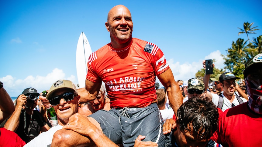 An American male surfer is carried on the shoulders of supporters after winning surfing event in Hawaii.