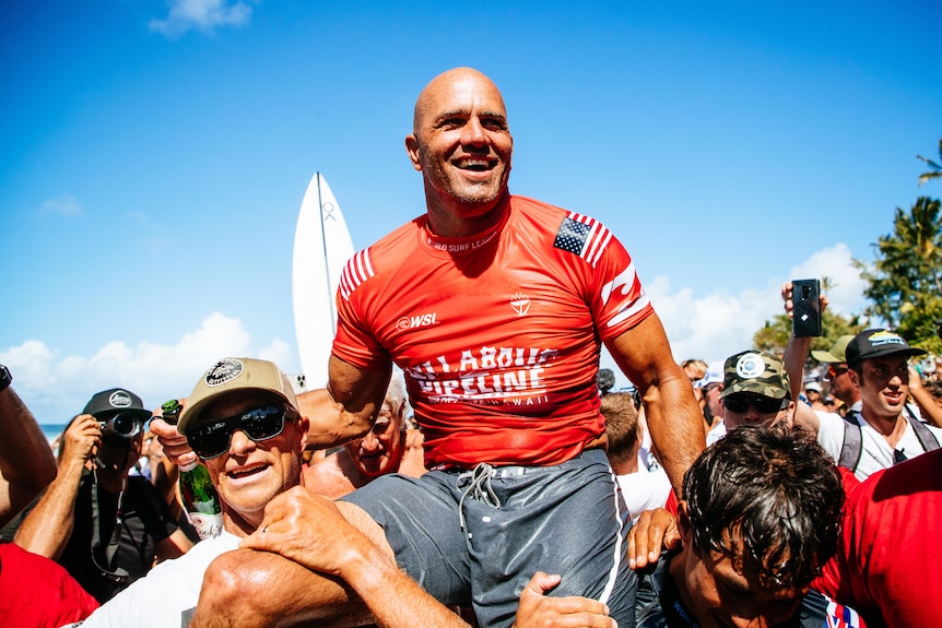 An American male surfer is carried on the shoulders of supporters after winning surfing event in Hawaii.