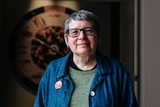 An Aboriginal woman with glasses and grey hair stands in front of projected artwork