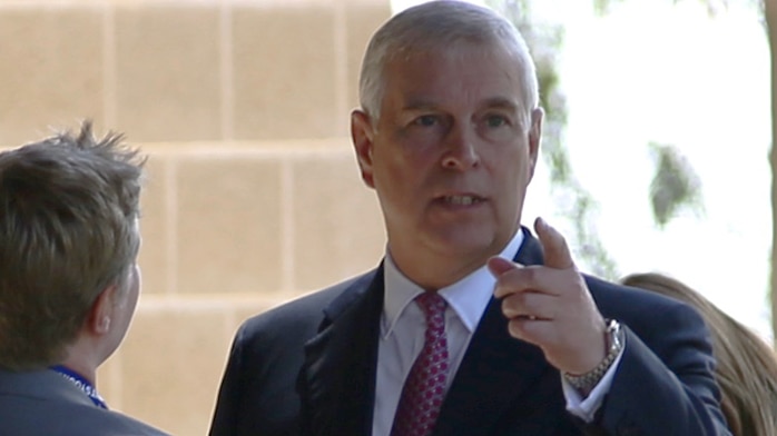 Prince Andrew greets some people in suits and points his finger towards something off camera.