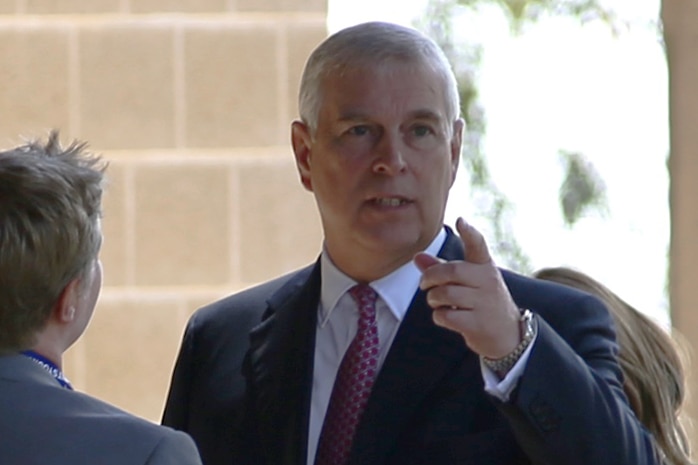 Prince Andrew greets some people in suits and points his finger towards something off camera.