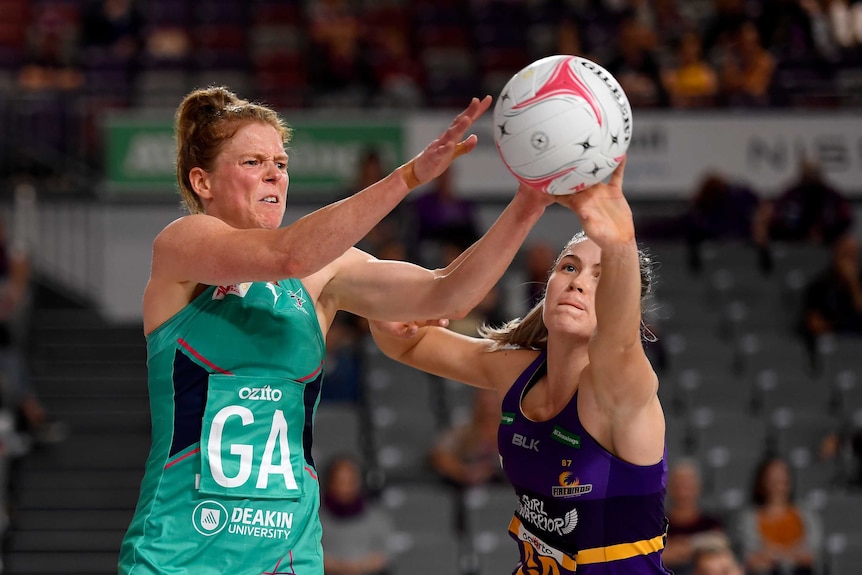 A Melbourne Vixens Super Netball player competes for the ball alongside a Queensland Firebirds opponent.