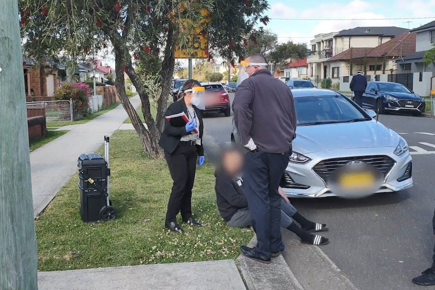 man sits in gutter surrounded by two standing police officers