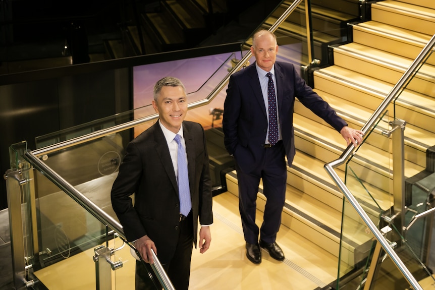 BHP CEO Mike Henry and CFO David Lamont stand on a staircase in a corporate office.
