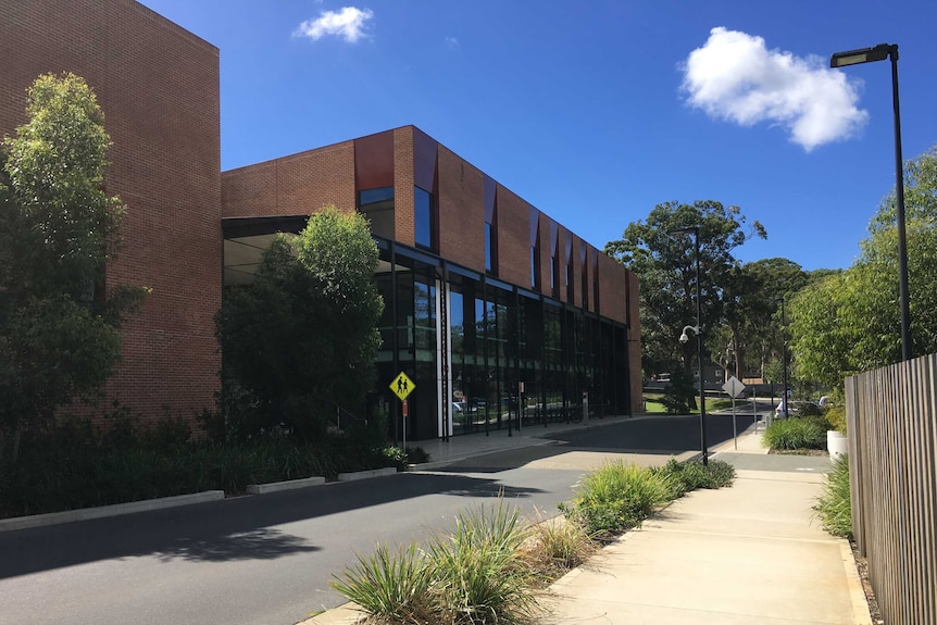 Exterior of a large university building and carpark on a sunny day.