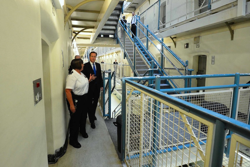 Former UK Prime Minister David Cameron walks down prison corridor with a female member of staff.