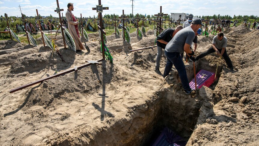 volunteers lower a coffin into a grave in Bucha, in the Kyiv region