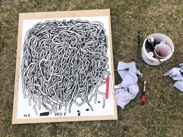 Ein Schwarz-Weiß-Gemälde, das auf Gras sitzt, mit einem Eimer Wasser und daneben sitzen Pinsel