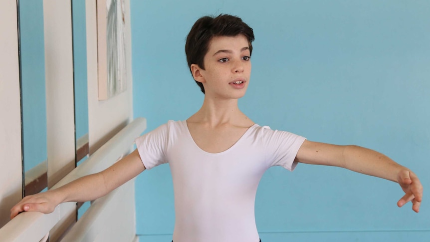 A young boy with his arms above his head, acting out a ballet stance in a hall room.