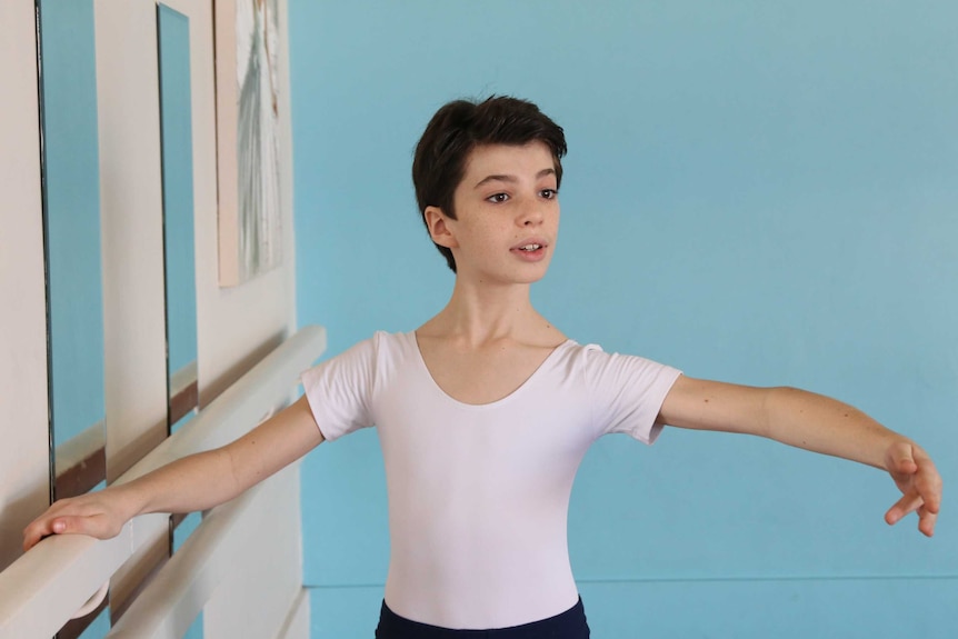 A young boy with his arms above his head, acting out a ballet stance in a hall room.