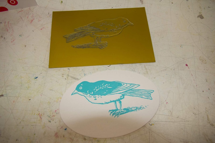 A printing plate of a bird with a paper print in blue ink made from the plate