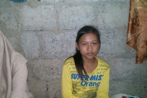 Reski Suci Ramdani, wearing a yellow t-shirt, sits next to someone in front a wall.