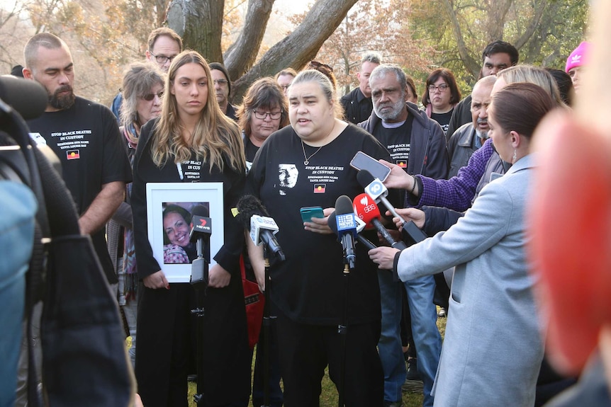 Apryl Watson, holding a photo of her mother, stands next to her sister Belinda Stevens as they speak to media.