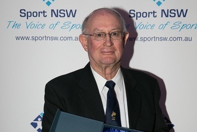 Dr Kellaher stands before a banner holding a trophy he's won