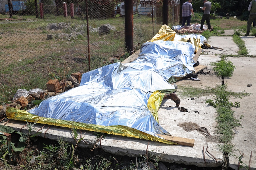 Investigators examine bodies covered by plastic sheeting of military prisoners at a prison in Olenivka.