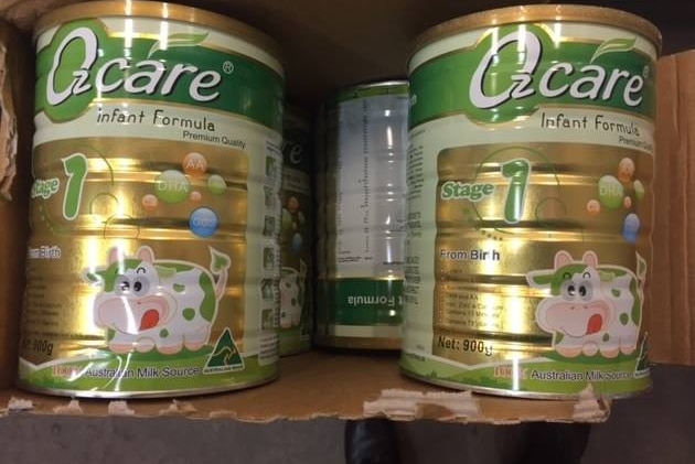 Several tins of Ozcare infant formula in a cardboard box.
