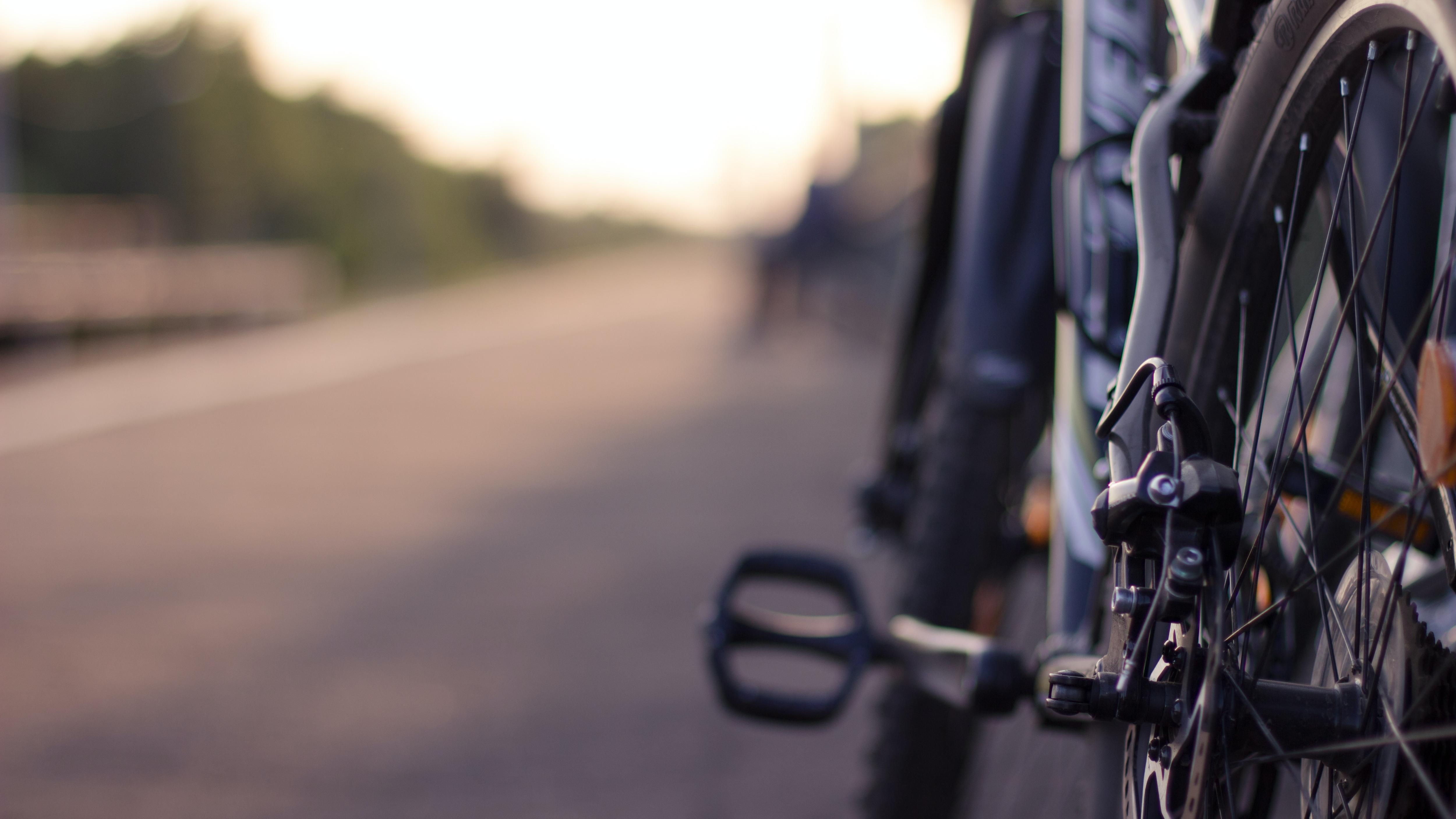 A close up of the back wheel of a bike, with country road out of focus in the background.