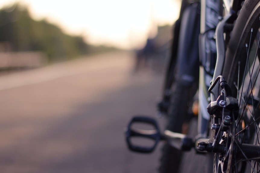 A close up of the back wheel of a bike, with country road out of focus in the background.