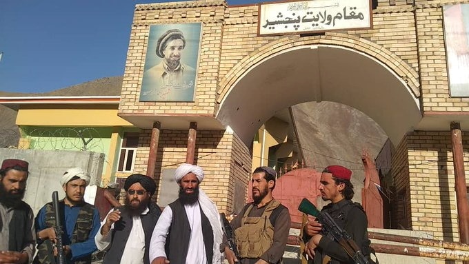 Taliban men outside a brick building. 