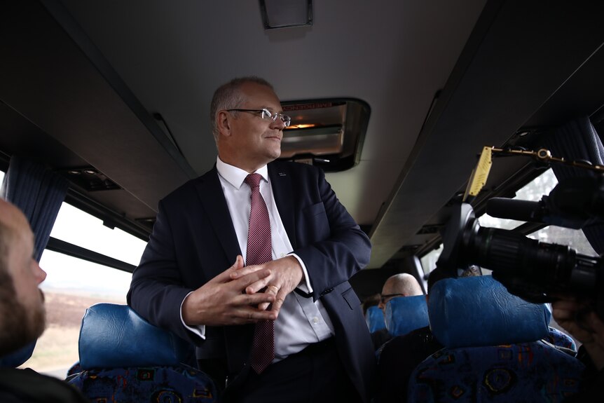 Scott Morrison leans on a seat inside a bus while a camera films him.