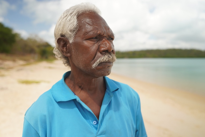 Indigenous man looks pensively into the distance as he walks along the beach