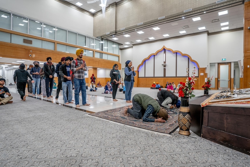 Two people kneel and place their faces on the floor as a queue of people lines up behind them.