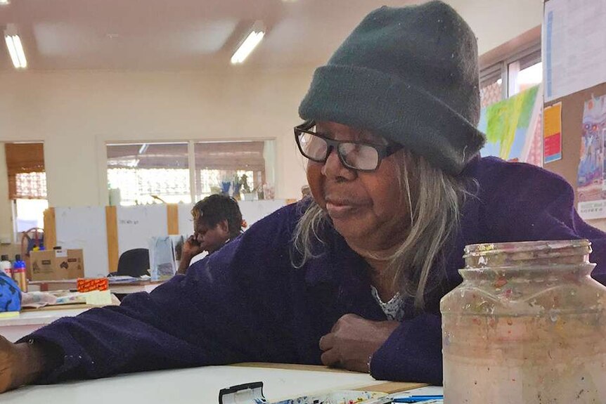 An Indigenous woman wearing a beanie, sitting at a table painting.