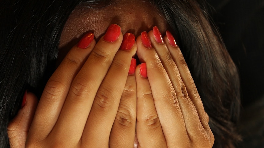 A woman with red fingernails holds her hands up over to cover her face