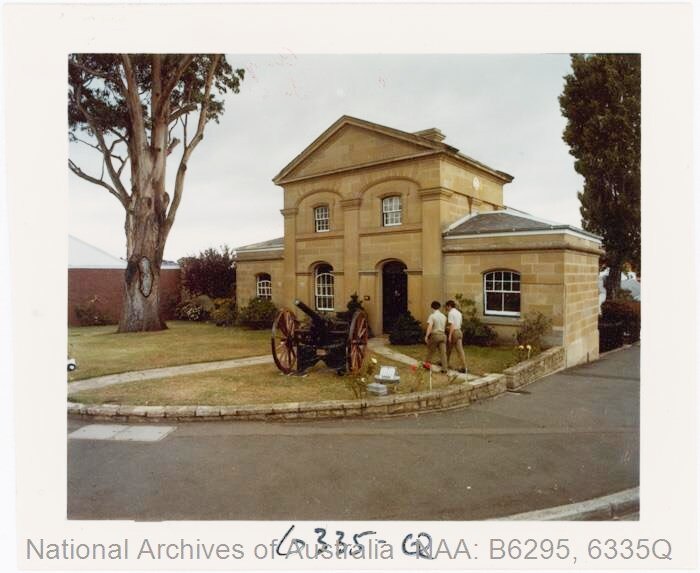 Photo of sandstone building with canon at front. Tree in left corner with concrete in it.