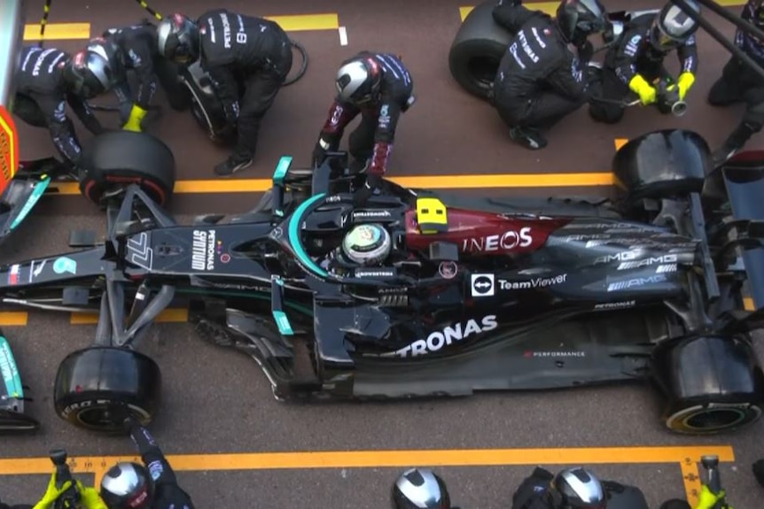 Pit crew try to remove tyres from a race car.