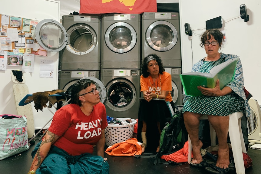 Three women sit in laundry while one reads stories.