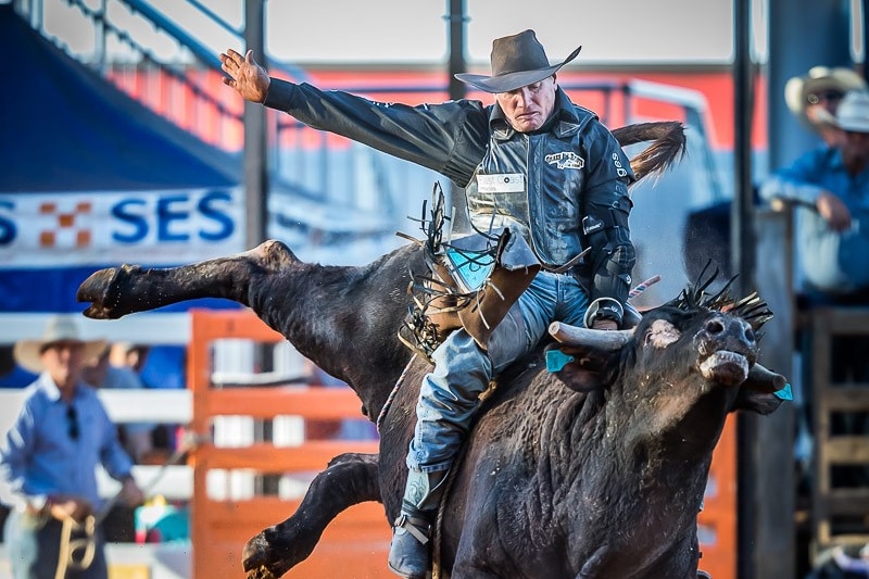 Bull-rider Dave Mawhinney rides a bucking bull in a rodeo arena.