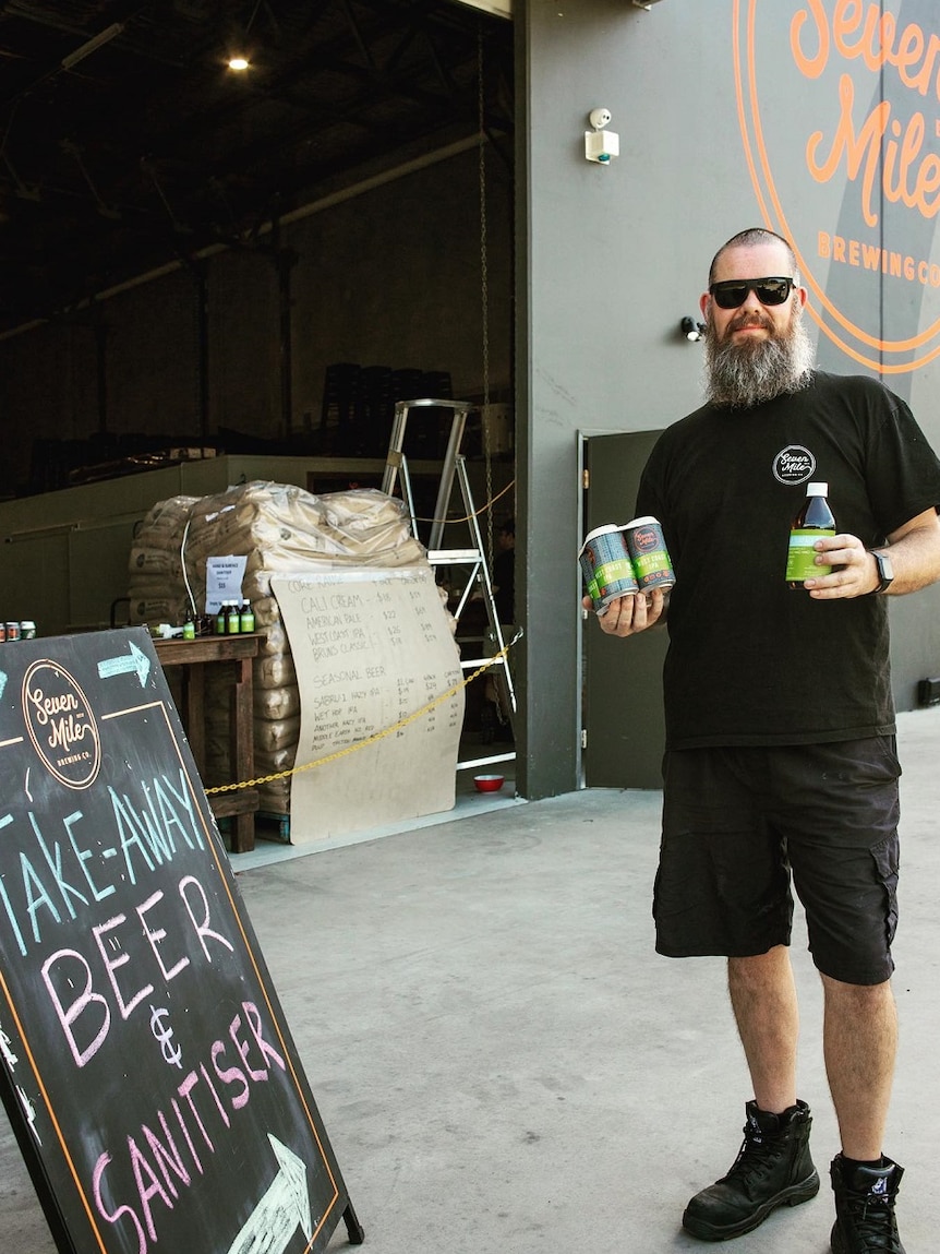 A brewery employee holds a four pack of canned beers and a bottle of hand sanitiser.