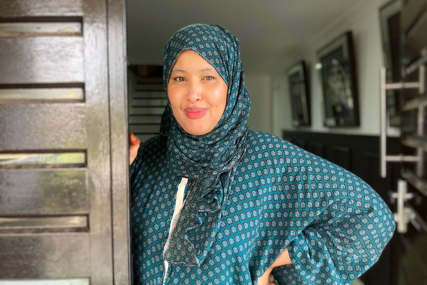 A woman wearing a headscarf standing beside a door. 