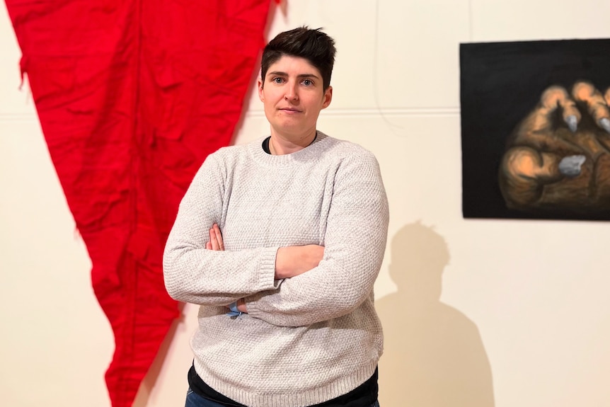 A woman with her arms crossed stands beside a large red piece of fabric pinned to a wall. 